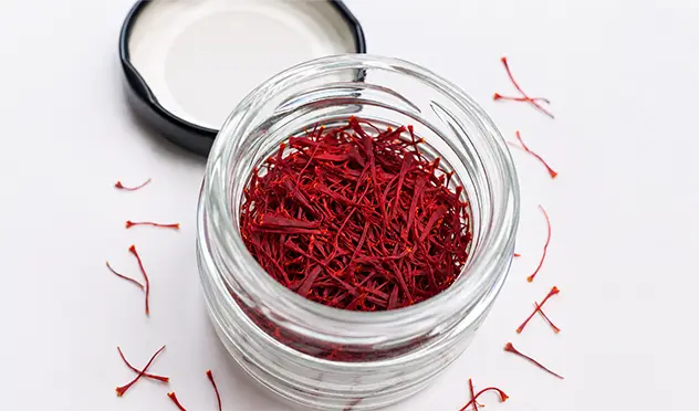 Close-up of authentic mongra saffron threads in a glass jar on a white background